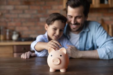Close up of dad and son save money in piggybank