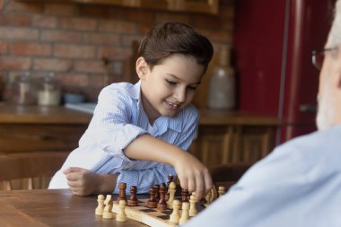 Small grandson play chess with mature grandfather at home