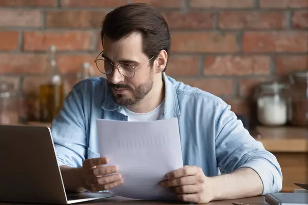 Serious millennial man work on laptop with paperwork — Zdjęcie stockowe