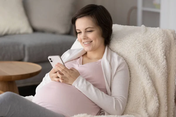 Gelukkig jong zwanger vrouw genieten van vrije tijd thuis, met behulp van smartphone — Stockfoto