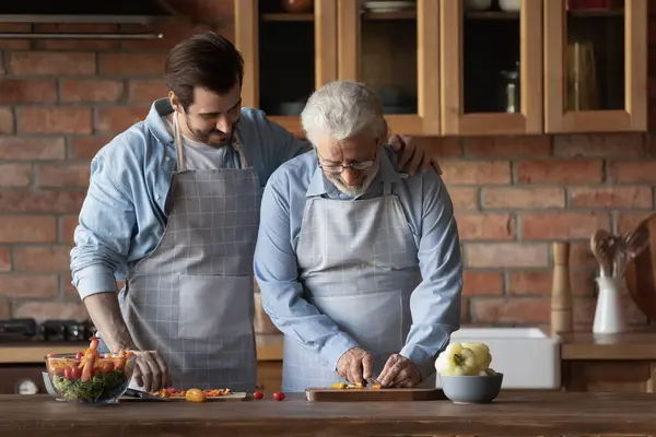 Caring grownup son and mature dad cooking together — Stockfoto