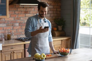 Smiling Caucasian man cook with recipe on cellphone
