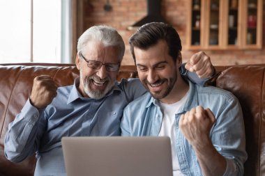 Smiling adult son and old father celebrate online win