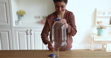 Smiling Indian woman holds plastic bottle pouring water into glass