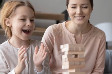 Overjoyed mother and small daughter play wooden game together