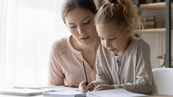 Loving mother help small daughter with homework assignment — ストック写真