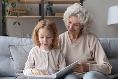 Loving grandmother read book with small granddaughter