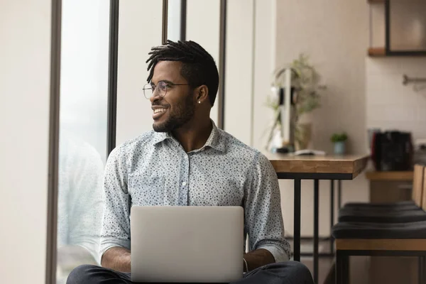Distracted from laptop work African hipster guy looks out window — Stockfoto