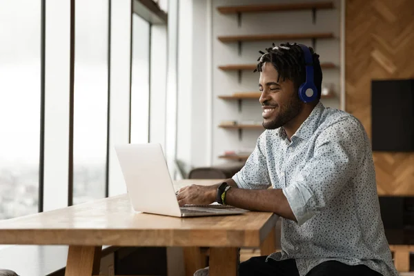 African guy using laptop listens audio course through headphones