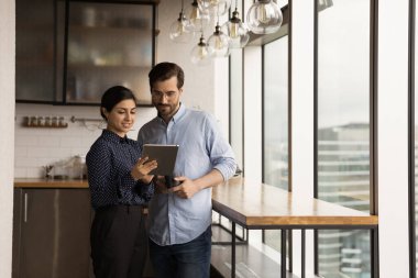 Diverse colleagues during workday lunch break using tablet discuss project