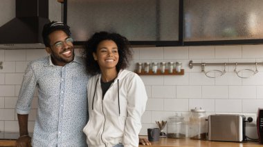 Happy African couple standing in kitchen smile looking into distance