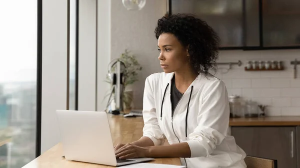 Pensive African female distracted from laptop work looks into distance — ストック写真