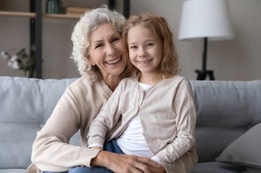 Portrait of happy old grandmother and small granddaughter on sofa