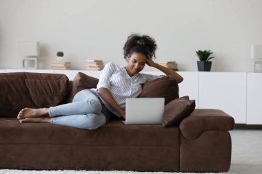 Happy ethnic woman relax on sofa using laptop