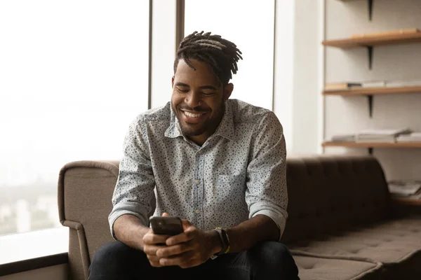 African man smiling look at smartphone chatting online — Stok fotoğraf