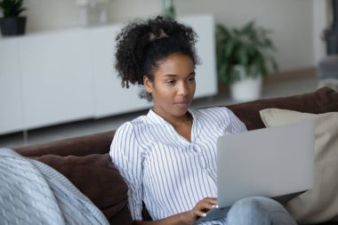 Happy ethnic woman relax on sofa working on laptop