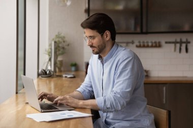 Serious male entrepreneur sit at table working using laptop