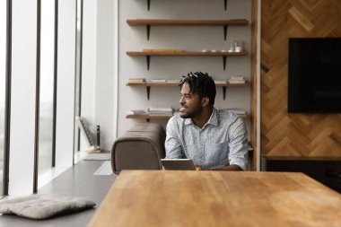 African guy hold tablet look aside, daydreams about career growth