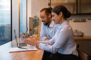 Multiracial colleagues sit in modern office kitchen working use laptop