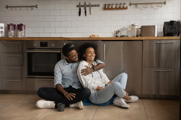 African millennial couple sit on floor in the kitchen