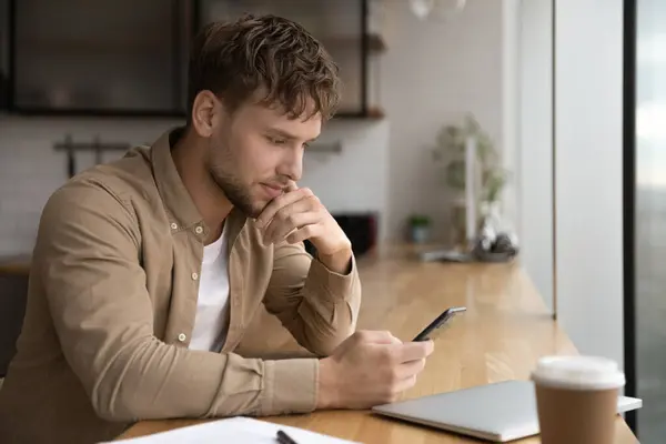 Serious young 30s man sit indoor with smartphone — Fotografia de Stock