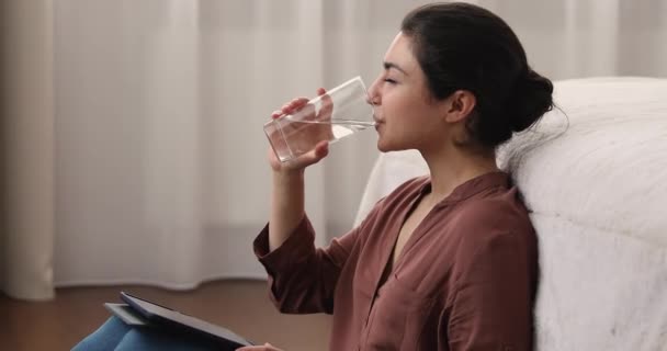Νεαρή Ινδή γυναίκα πόσιμο νερό, ενώ κρατώντας ψηφιακό δισκίο — Αρχείο Βίντεο