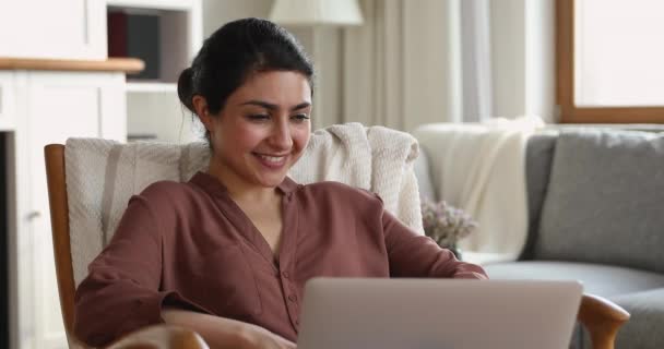 迷人而宁静的印度女人，靠着笔记本电脑坐在舒适的扶手椅上放松 — 图库视频影像