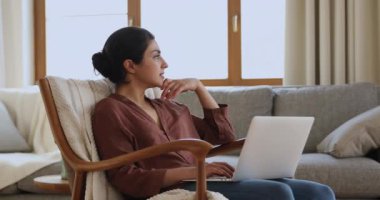 Indian woman sit on comfy armchair working on laptop