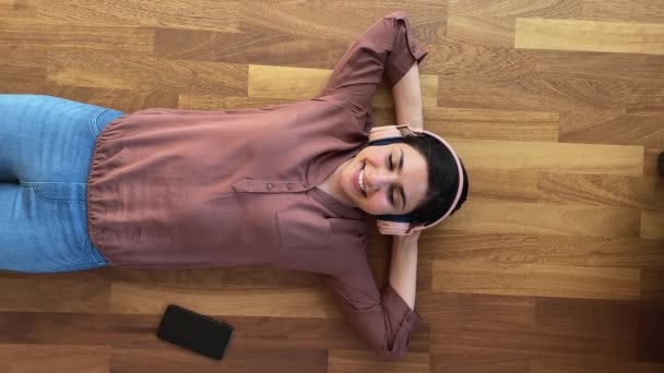 Расслабленная индийская женщина лежит на полу слушать музыку через наушники — стоковое видео