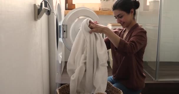 Indian housewife doing housework putting bath towels into washing machine — Stockvideo