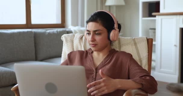 Indian woman wear headphones talk through video conference using laptop — Video