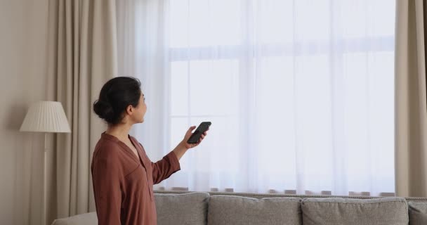 Indian woman close blinds indoor holds cellphone use smarthome app — Vídeo de Stock