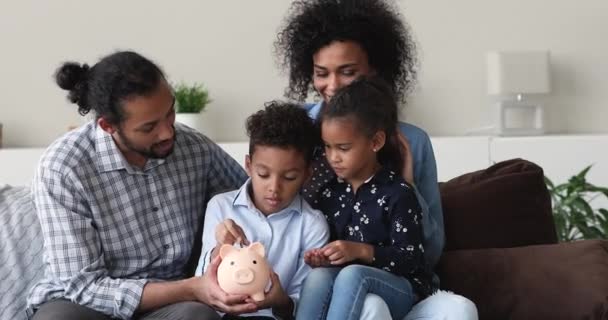 Smiling young african american parents teaching kids saving money. — Stockvideo