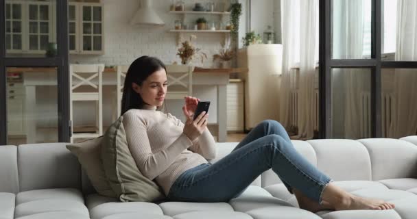 Relaxé jeune femme heureuse en utilisant smartphone à la maison. — Video