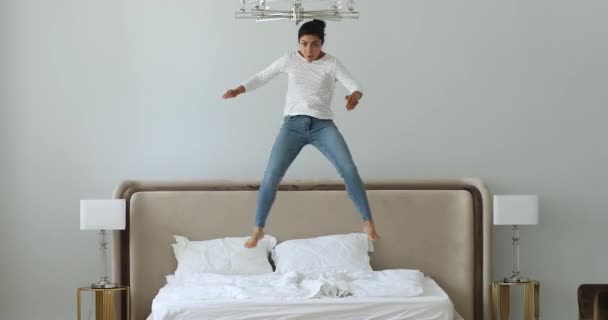 Full-length untroubled Indian woman in casual clothes jumping on bed — Stock Video