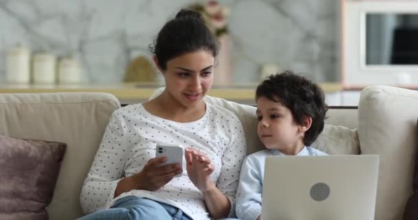 Mulher indiana seu filho sentado no sofá usando diversos gadgets — Vídeo de Stock