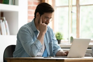 Ciddi bir adam masada oturup dizüstü bilgisayarına bakar e-postaları okur.