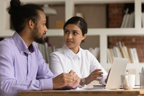 Two multiethnic colleagues sit at desk communicating discuss current business — Stock Photo, Image