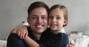 Sevgi dolu genç bir baba gülümseyen küçük bir kızı kucaklıyor.