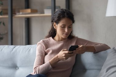 Ciddi bir kadın kanepeye oturur cep telefonu uygulamaları kullanır.