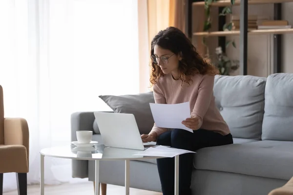 Serious Latina woman holds papers makes online payment use laptop — Stock Photo, Image