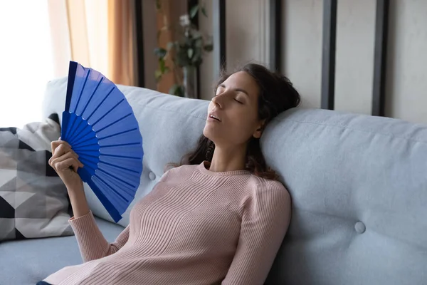 Overheated woman sit on sofa wave hand fan reduce heat