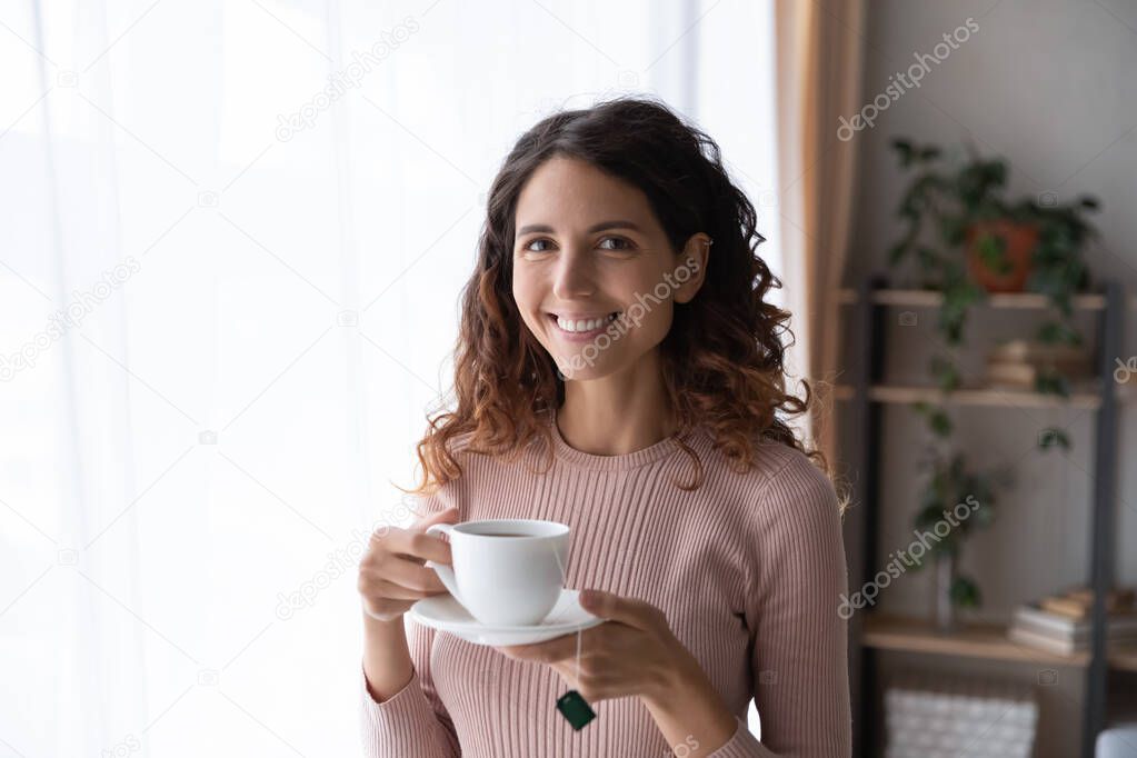 Woman standing indoor holding cup of fresh brewed tea