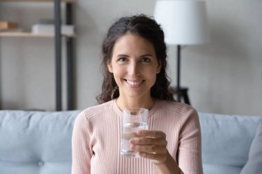 Latin genç kadın elinde bir bardak suyla kanepede oturuyor.