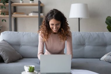 Neşeli Latin kadın kanepede oturur dizüstü bilgisayarla mesaj atar.