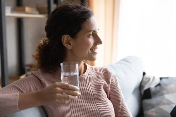 Woman sit indoor holding glass of water looks into distance — Stock Photo, Image