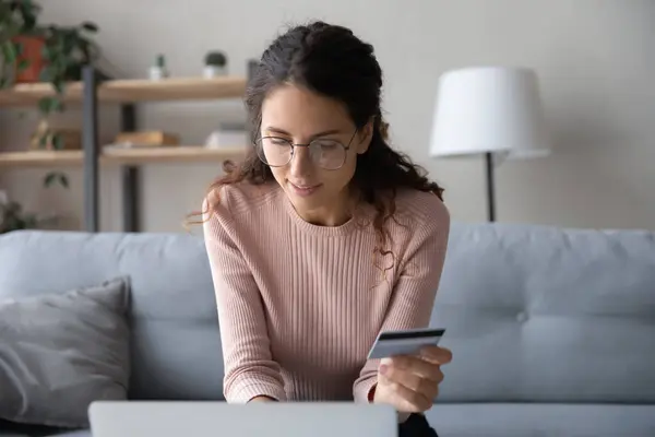 Woman sit on sofa holds credit card makes secure e-payment — Stock Photo, Image