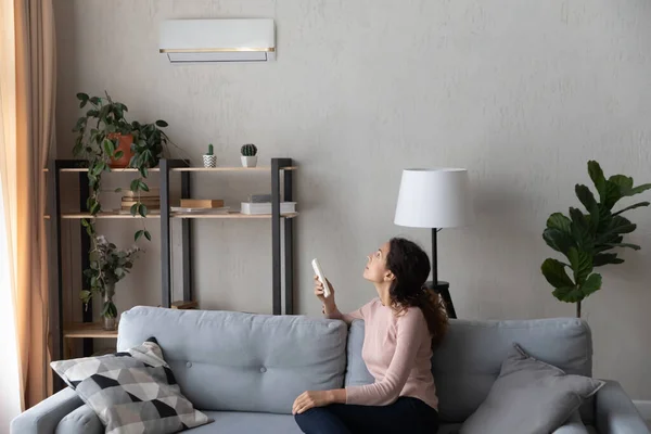 Femme assise sur le canapé tenant la télécommande allume le climatiseur — Photo