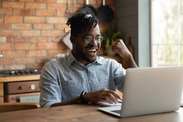 Aufgeregter afrikanischer Millennial-Kerl benutzt Laptop zu Hause — Stockfoto