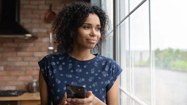 Happy pensive jonge Afro-Amerikaanse vrouw met smartphone weg te kijken — Stockfoto